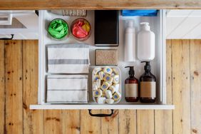 top view of opened drawer with towels, washing sponge, detergent bottles and dishwashing tablets in plastic box in modern kitchen cabinet in apartment, storage concept