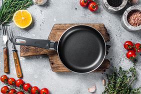 Various organic spices, herbs and ingredients around empty aged cooking skillet. Gray background.