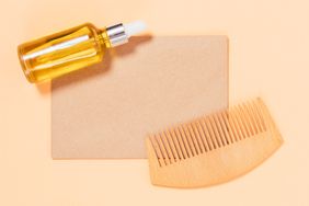 Natural hair care oil and wooden comb with blank card mockup on beige background,