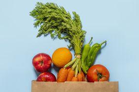 Directly above view of paper bag with fruit and vegetables on blue background