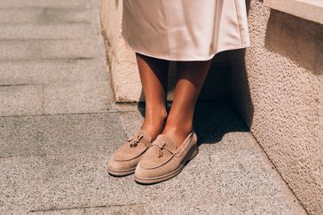 Portrait of fashionable women in beige dress and stylish suede loafer shoes posing in the street