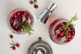 Cold refreshing drink with cranberries and rosemary on a white concrete background