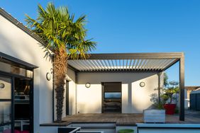 Trendy outdoor patio pergola. garden lounge, chairs, metal grill surrounded by landscaping