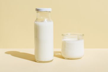 Bottle of organic fresh milk and glass of milk on beige background. Dairy, grow and drink concept. Minimal styl