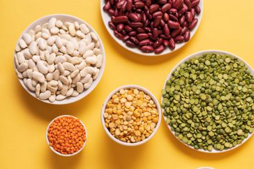 Top view of assortment of peas, lentils, beans and legumes over yellow background