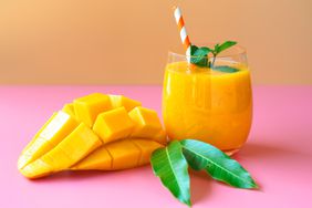 Mango smoothies topping with mint leaf on orange and pink background for summer fruit drink concept.