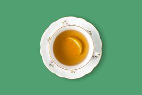 Cup of tea with lemon slice over green seamless background, copy space.