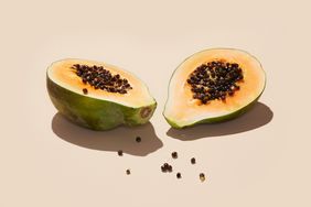 cut papaya on beige background with seeds spilling out onto surface