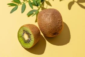 Fresh cut kiwi on isolated yellow background with shadow and leaves