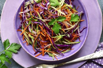 Red cabbage salad cole slaw with carrot and cucumber in a bowl on a dark grey slate, stone or concrete background