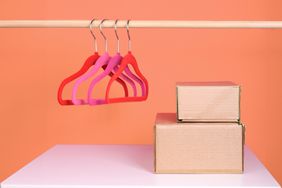 Clothes hangers and paper boxes on white table. Clothes hanging on rack in dressing room on pink.