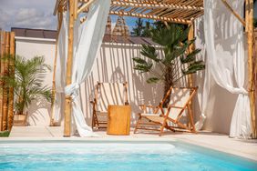 Boho Sun chairs under driftwood pergola by the swimming pool in warm sunlight