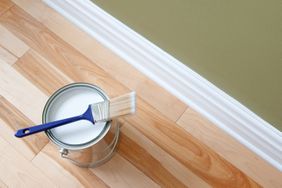 Newly opened can of white paint and paintbrush on wooden floor.