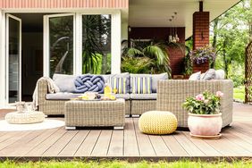 Garden table with fruits and fresh orange juice standing on wooden terrace with fresh plants, armchair and sofa with pillows