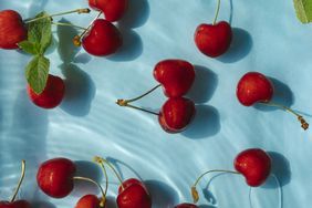 Red cherry berries and green mint leaves floating in water on blue background