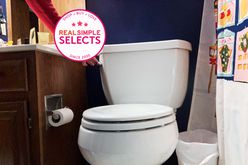 A person flushing the Kohler Highline Classic Pressure Toilet in a bathroom