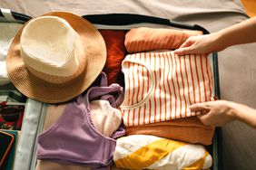 Person Packing Carry-On Suitcase with striped T-shirt, bathing suit, and hat 