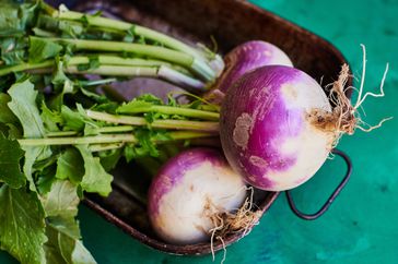 An overhead shot of fresh organic turnips on a wooden tray against a green surface